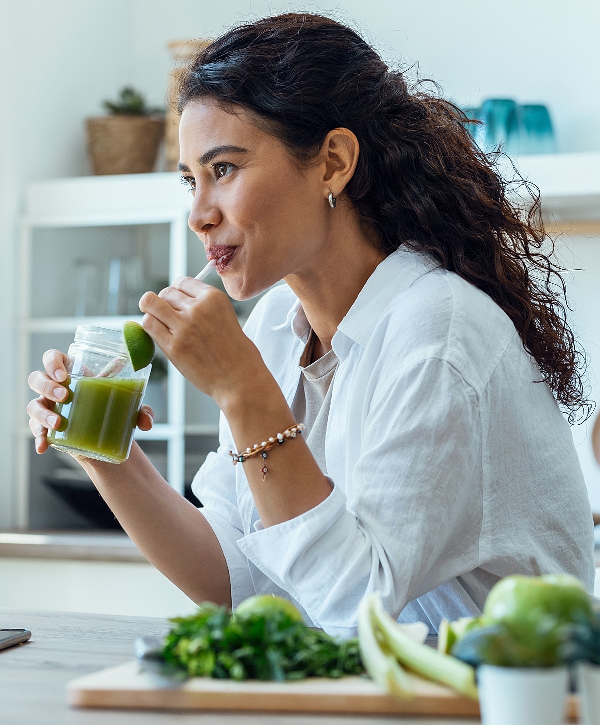 Woman enjoying a green smoothie in kitchen.