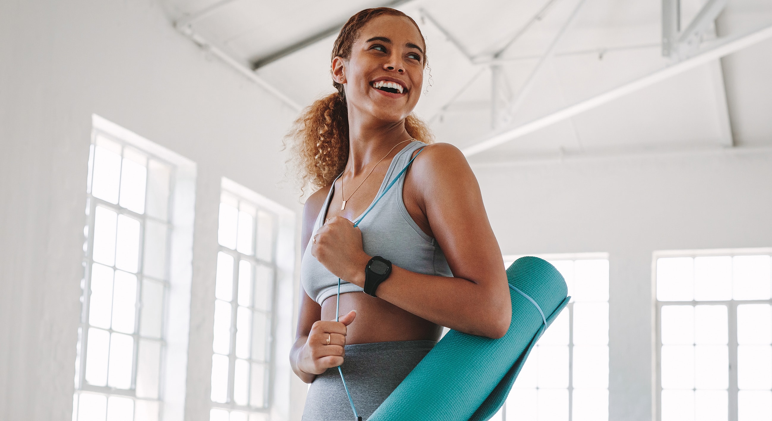 Smiling woman with yoga mat in studio.